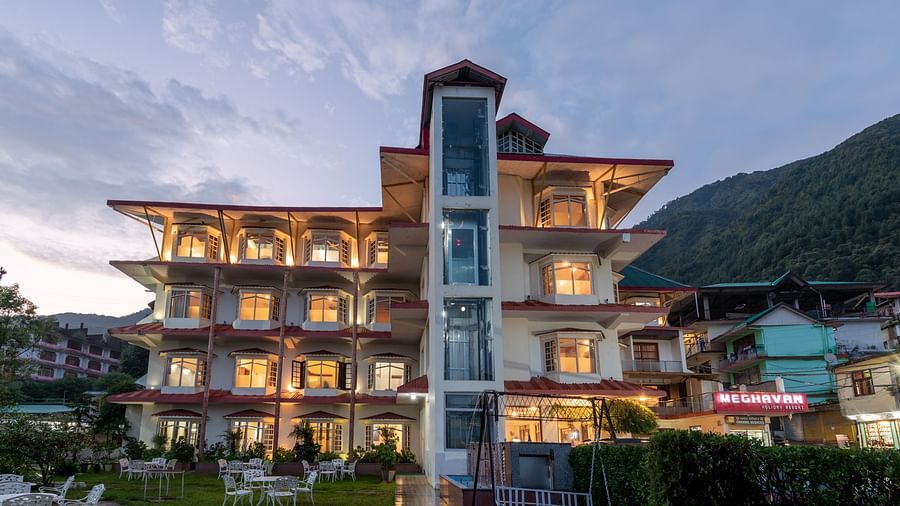 A well-lit hotel with a contemporary design, nestled amidst lush greenery and stunning mountain views - DLS Meghavan Resort